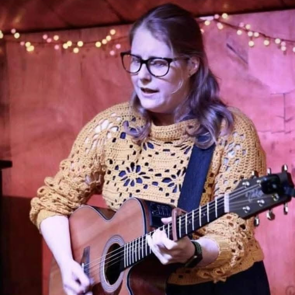 Clare Portman playing guitar with a warm, cosy background
