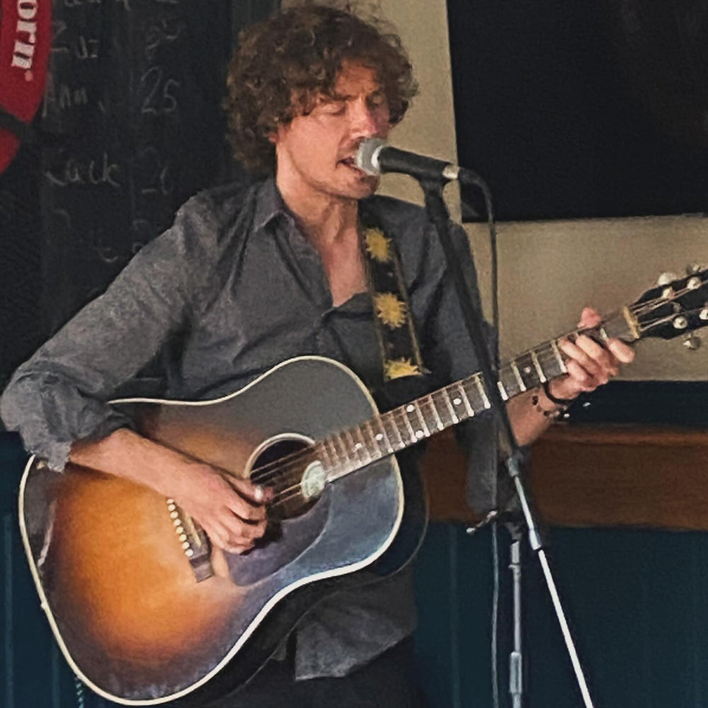 Jack Blackman playing an acoustic guitar in front of a microphone. Join us for an evening of live music Friday 29th August - 6–8pm
