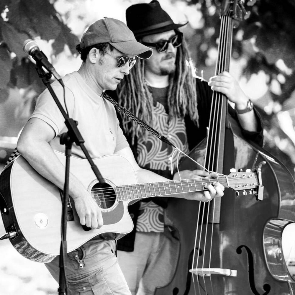 Two musicians from the brand Strum and Bass playing guitar and bass in a natural setting, to adversise their performance at 31 the cross worcester